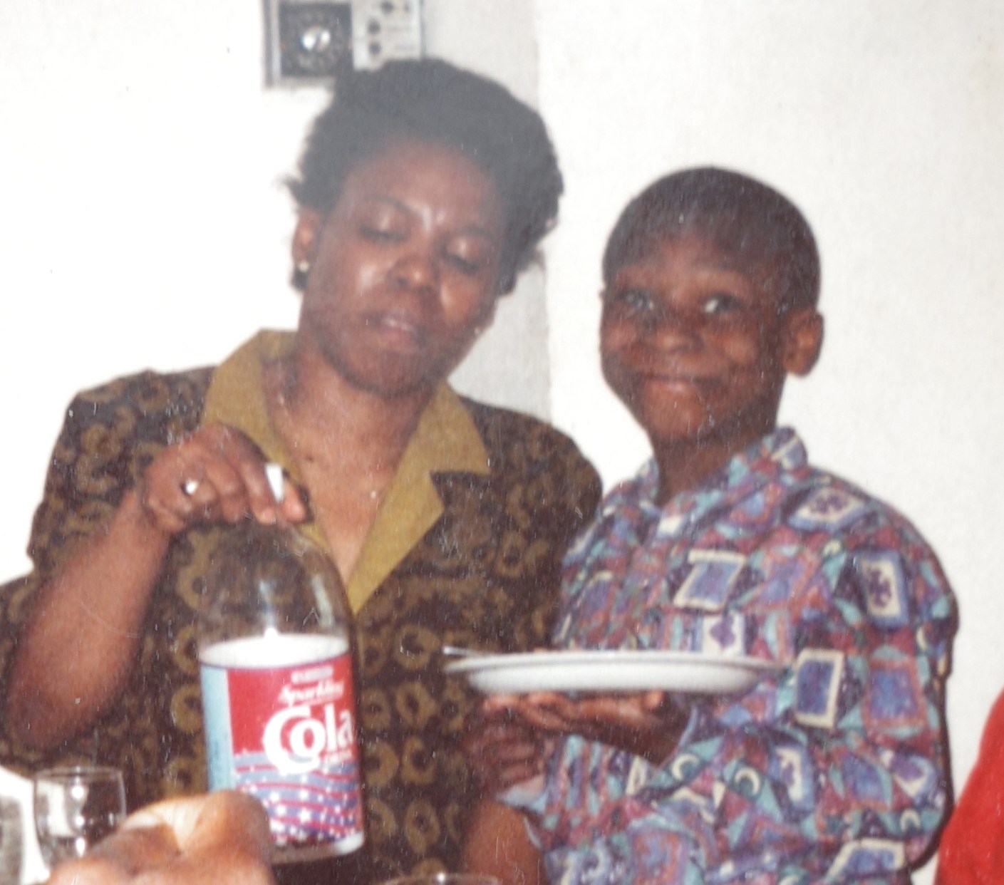 Photo of a woman and child at a table, the woman holding a bottle of cola.