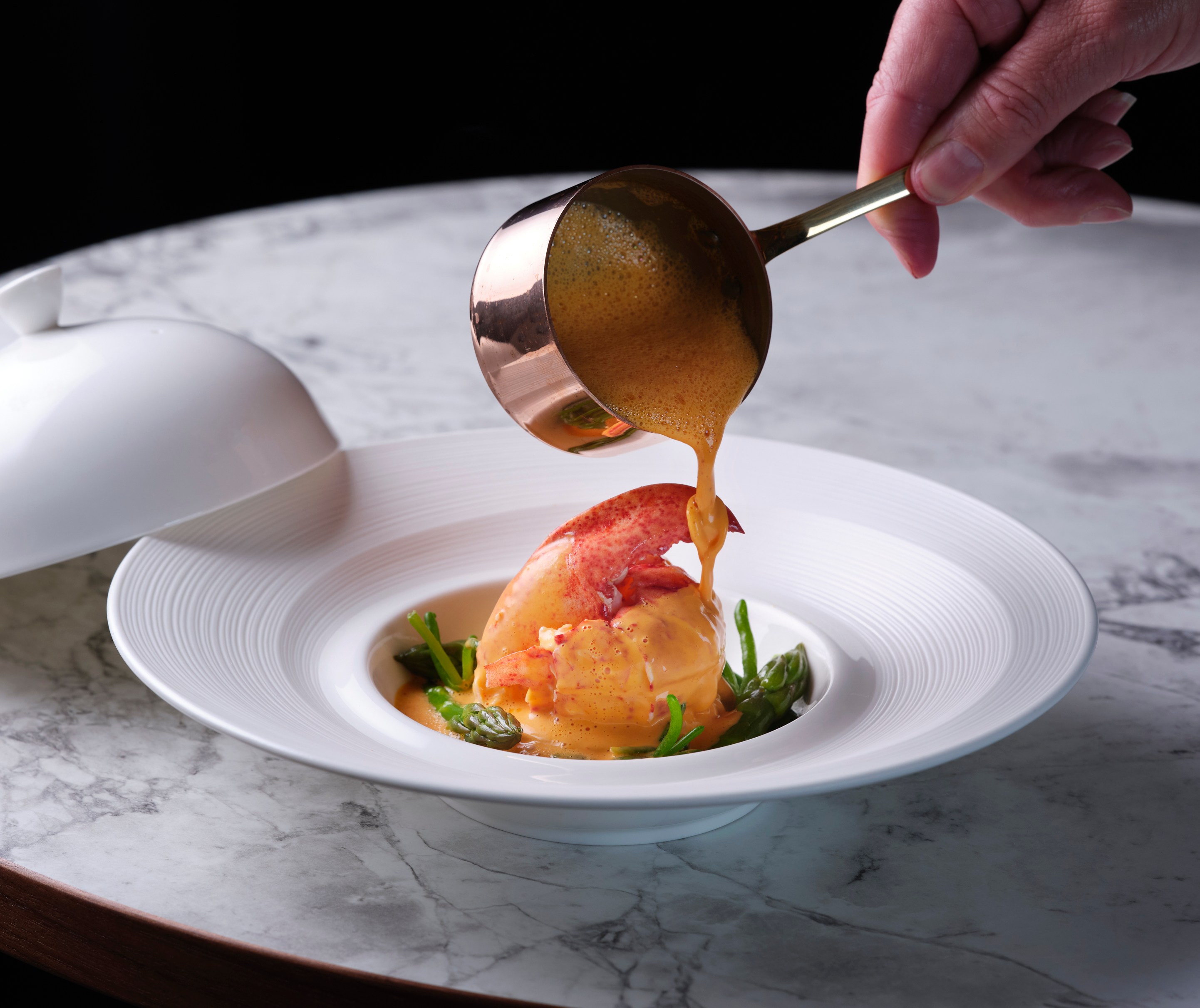Lobster dish with asparagus being drizzled with sauce.