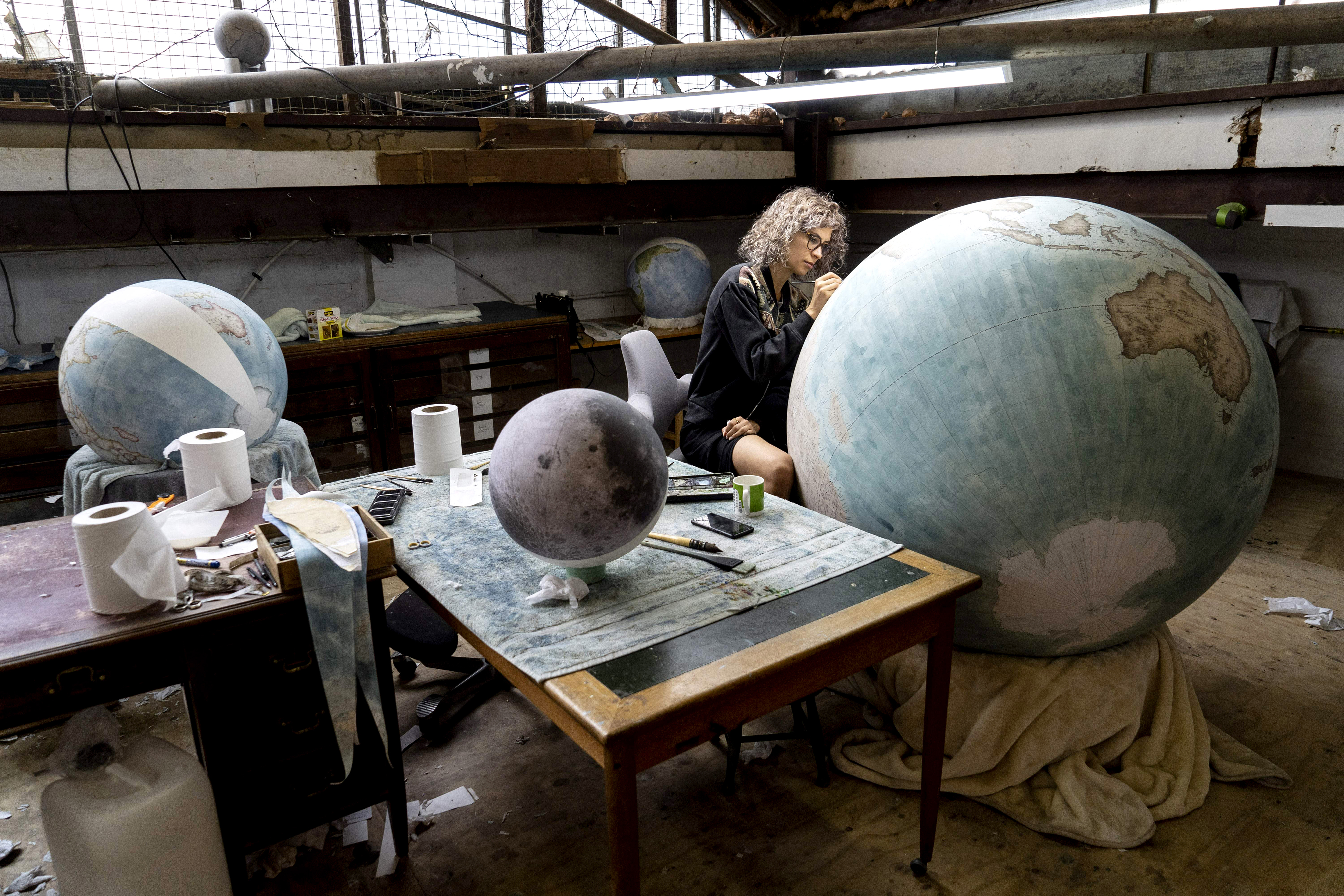 Artist painting a large globe in a workshop.