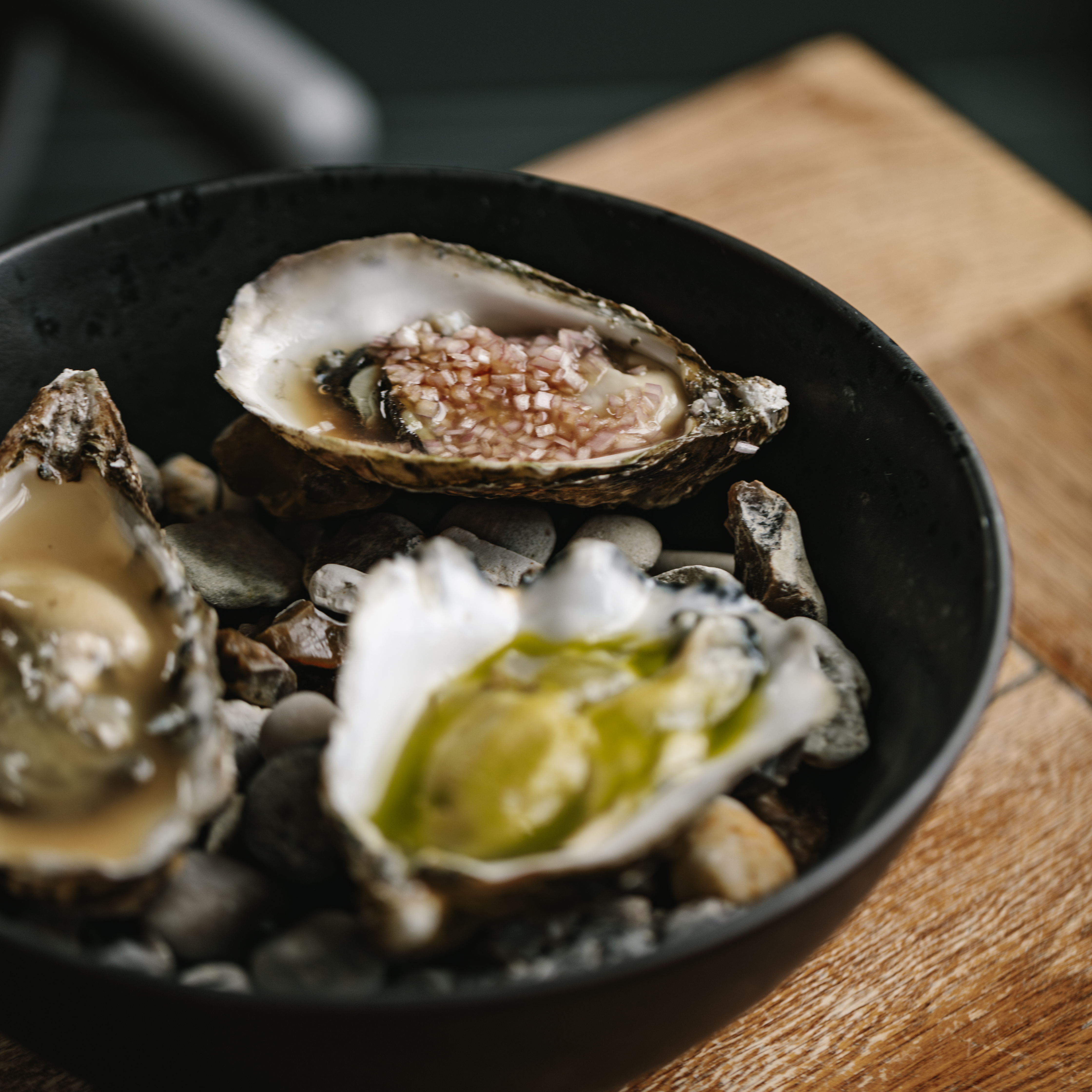 Three oysters on the half shell with different toppings in a black bowl.