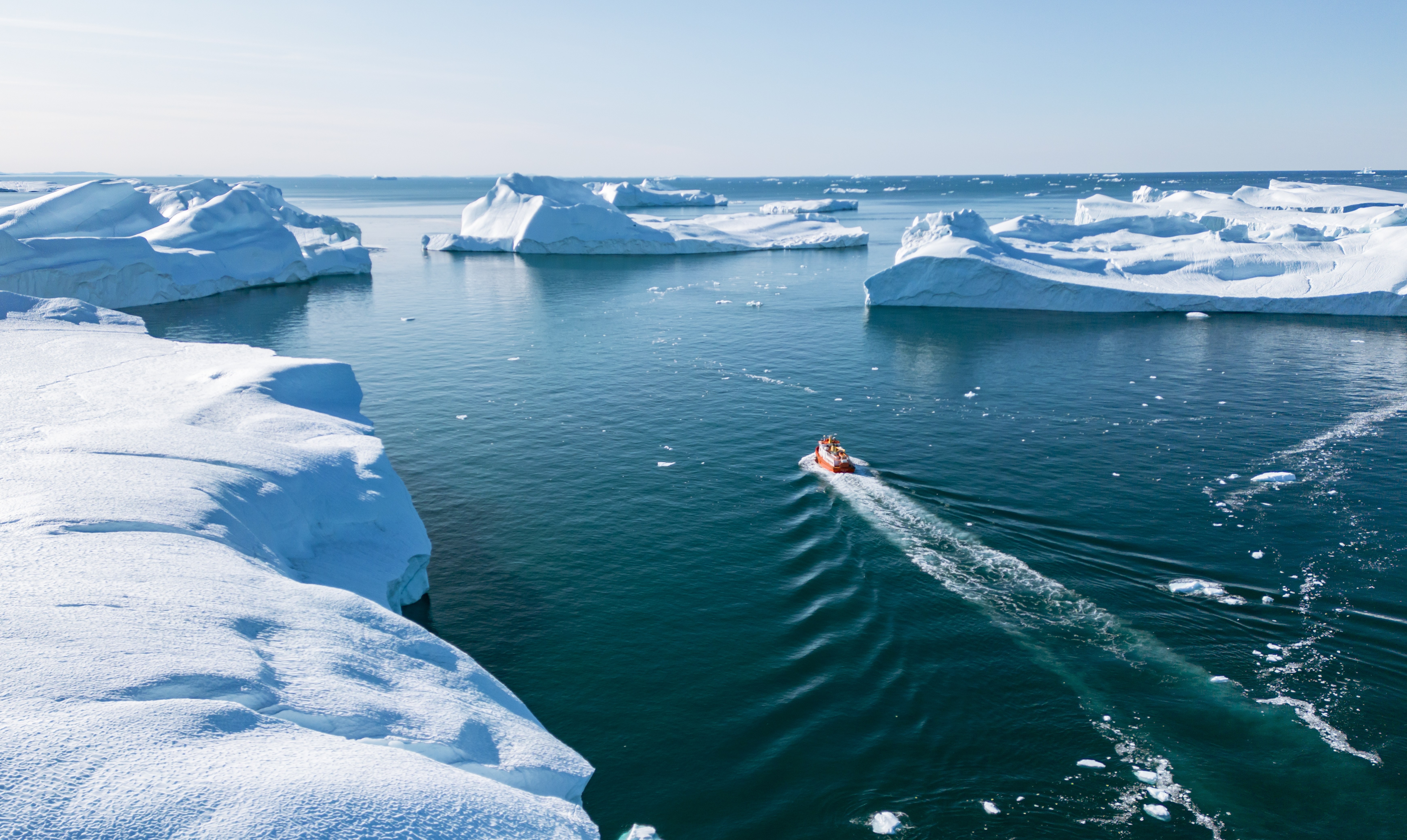 Aerial view of a boat navigating among icebergs in Ilulissat Icefjord, Greenland.
