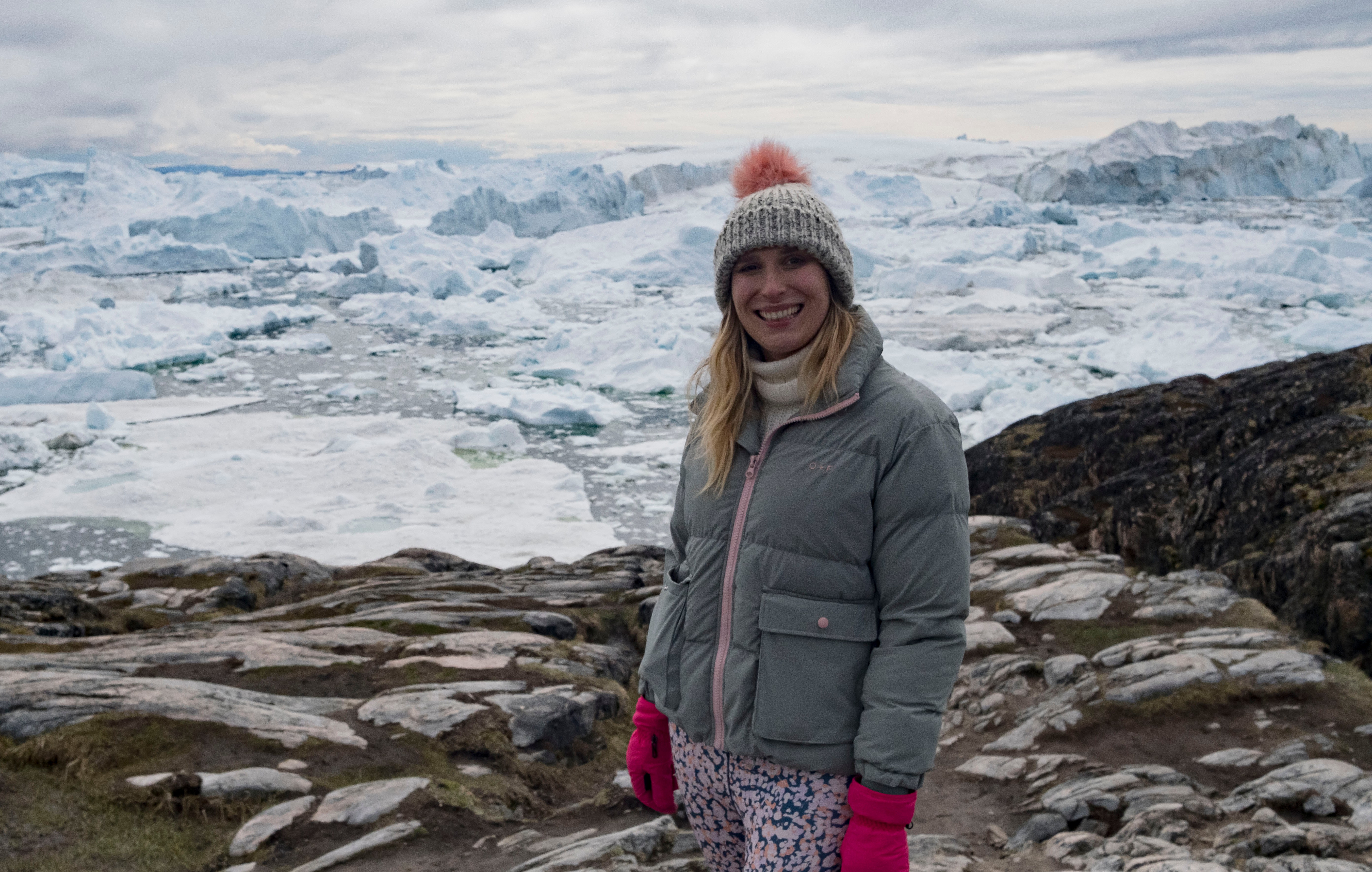 Woman in Greenland standing on rocky ground with icebergs in the background.