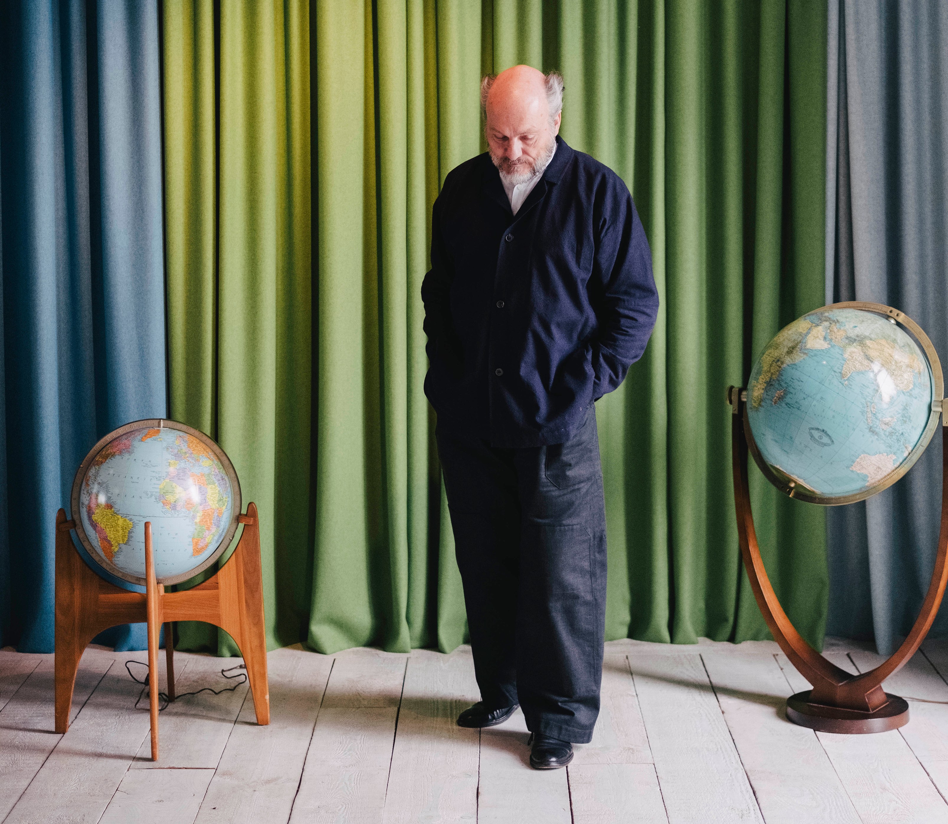 A man stands between two globes in front of green and blue curtains.